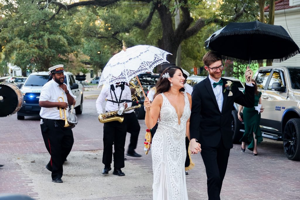 A bride & groom walking down a street in New Orleans holding umbrellas - Magnolia Ceremonies